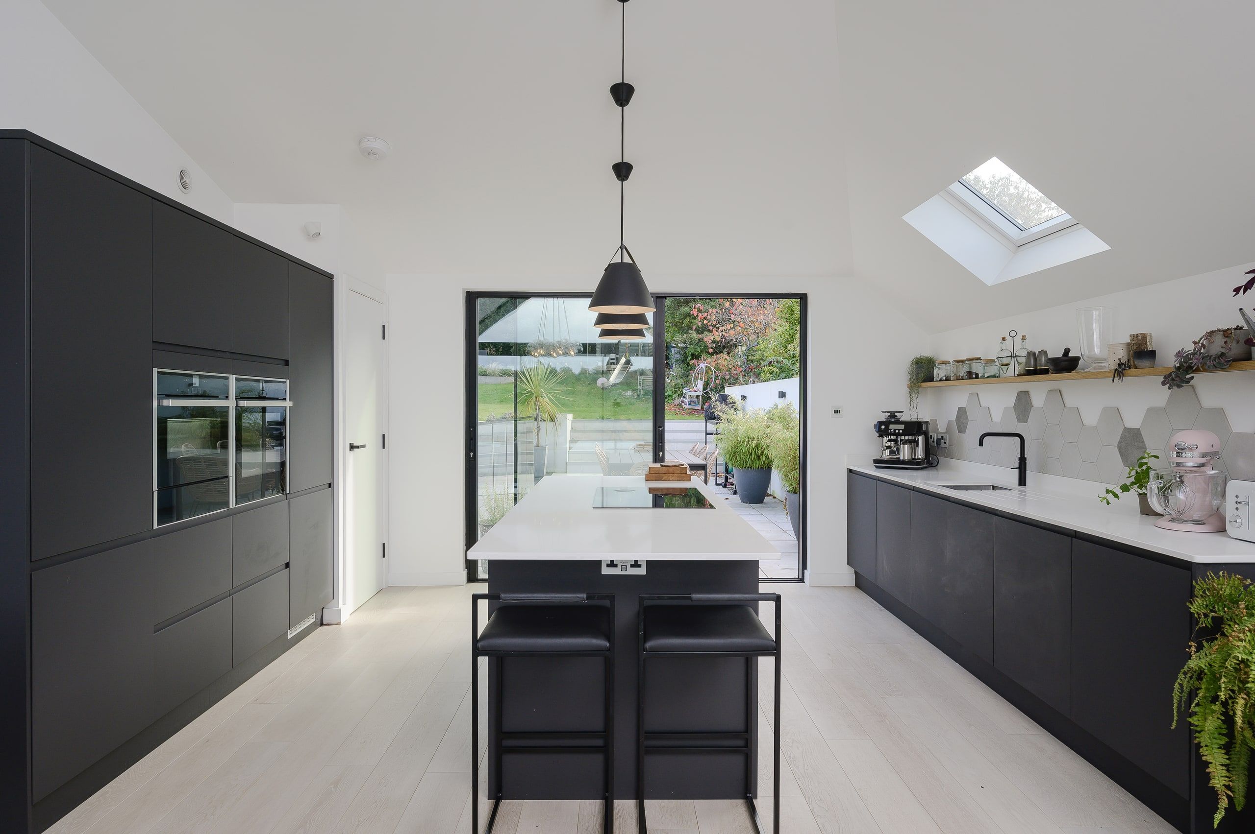 Dark grey kitchen with a white island and sliding doors onto the terrace, upside down house, Haslemere.