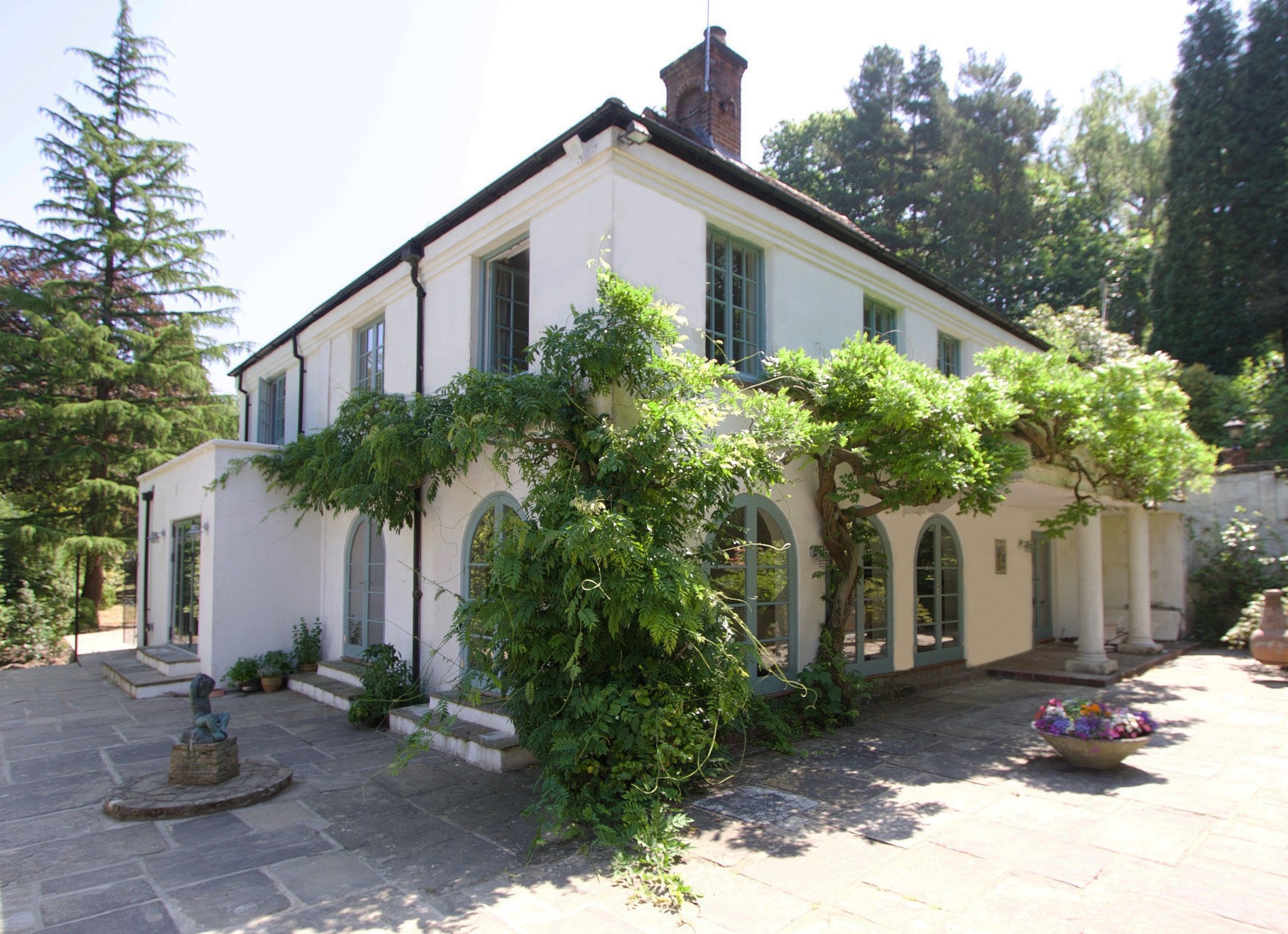 Wisteria over the arched loggia and stone terrace on the garden elevation, 1930s country house, Mole Valley.