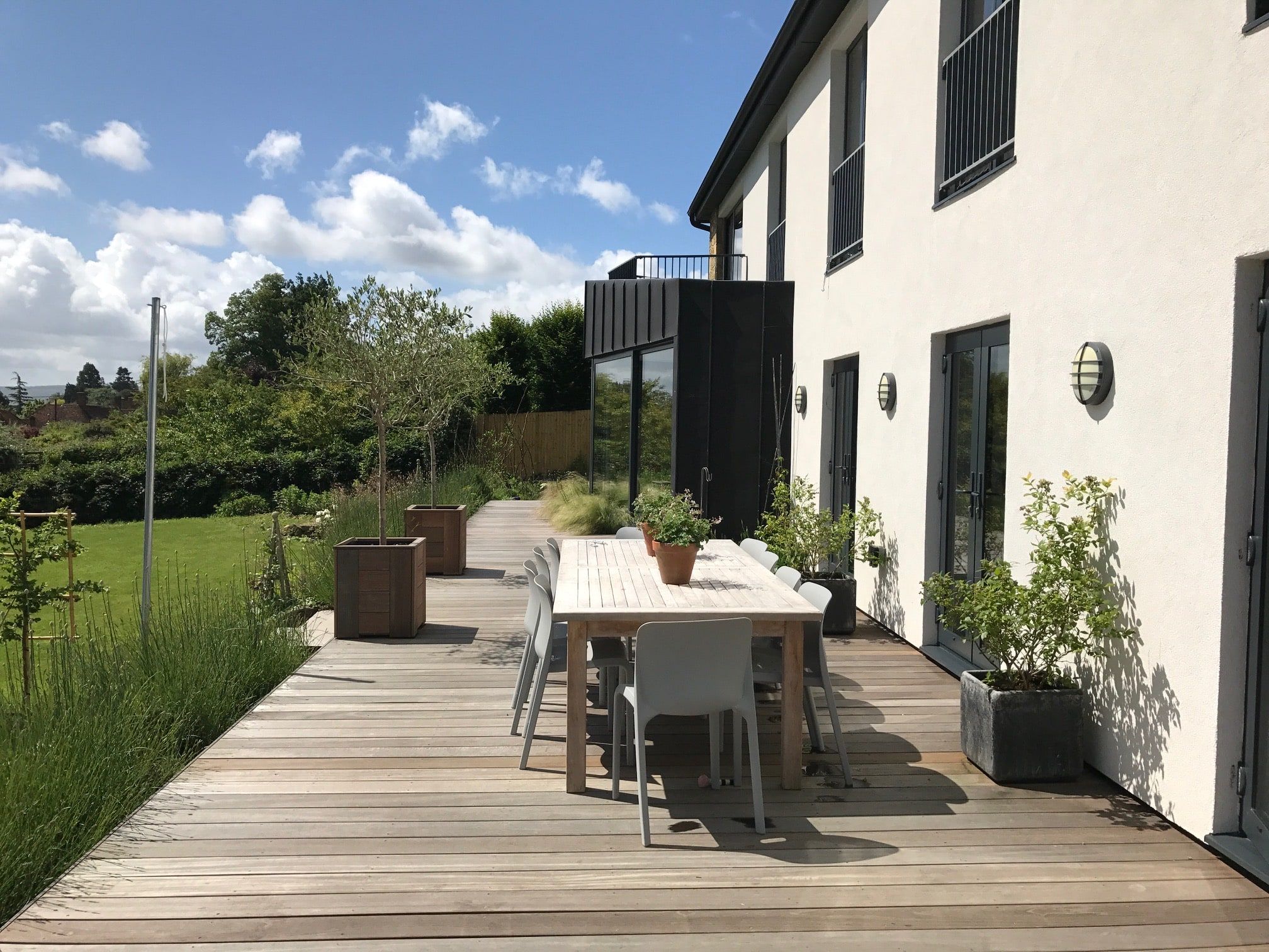 Timber deck terrace and dining table below the zinc-clad bay, with South Downs views, 1960s house, Lodsworth.