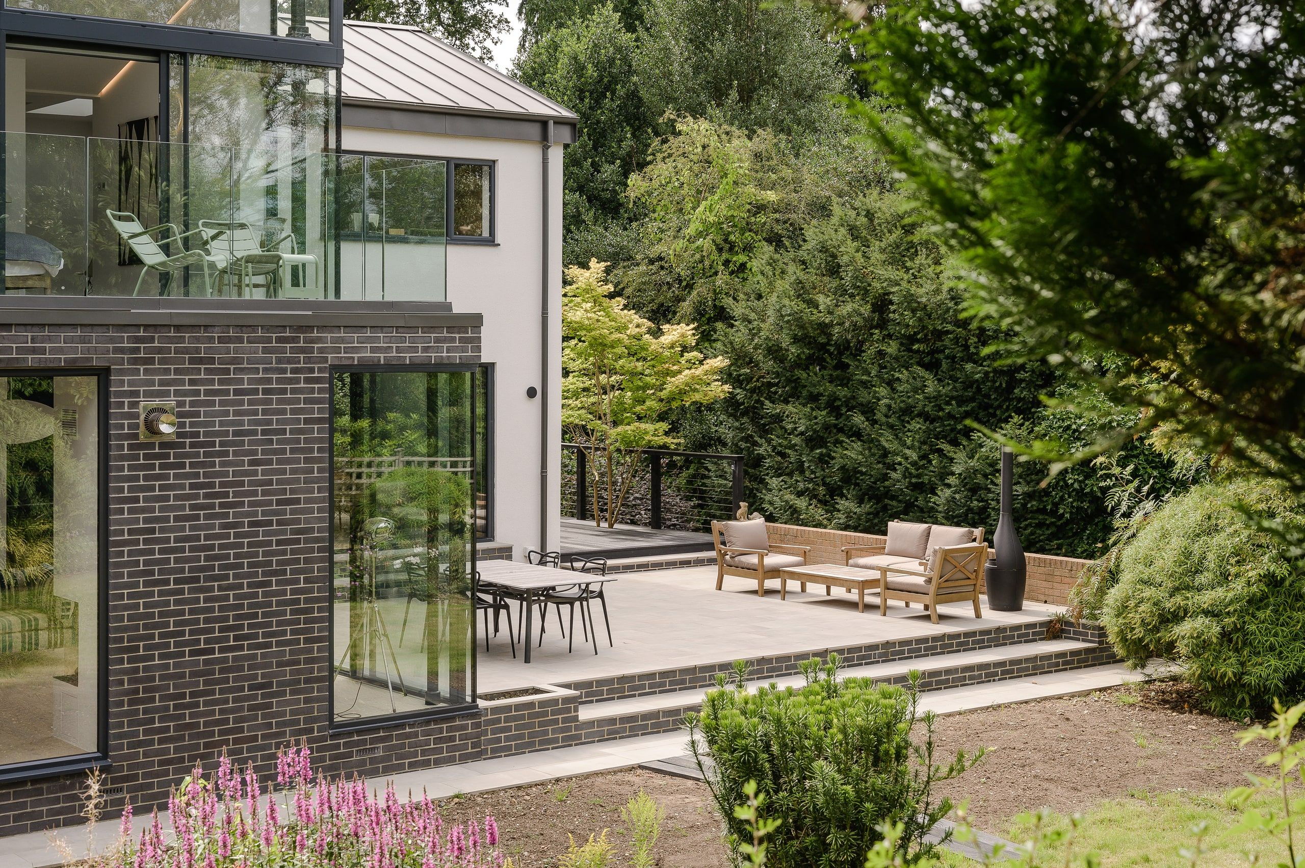 Corner window in the dark brick extension overlooking the terrace and garden seating, 1960s house, Haslemere