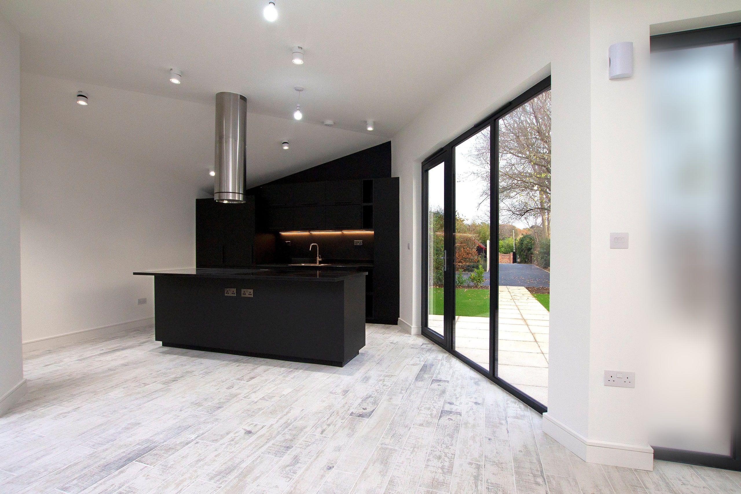 Open-plan kitchen and living space with a black island and stainless steel extractor, new build retirement house, Fareham.