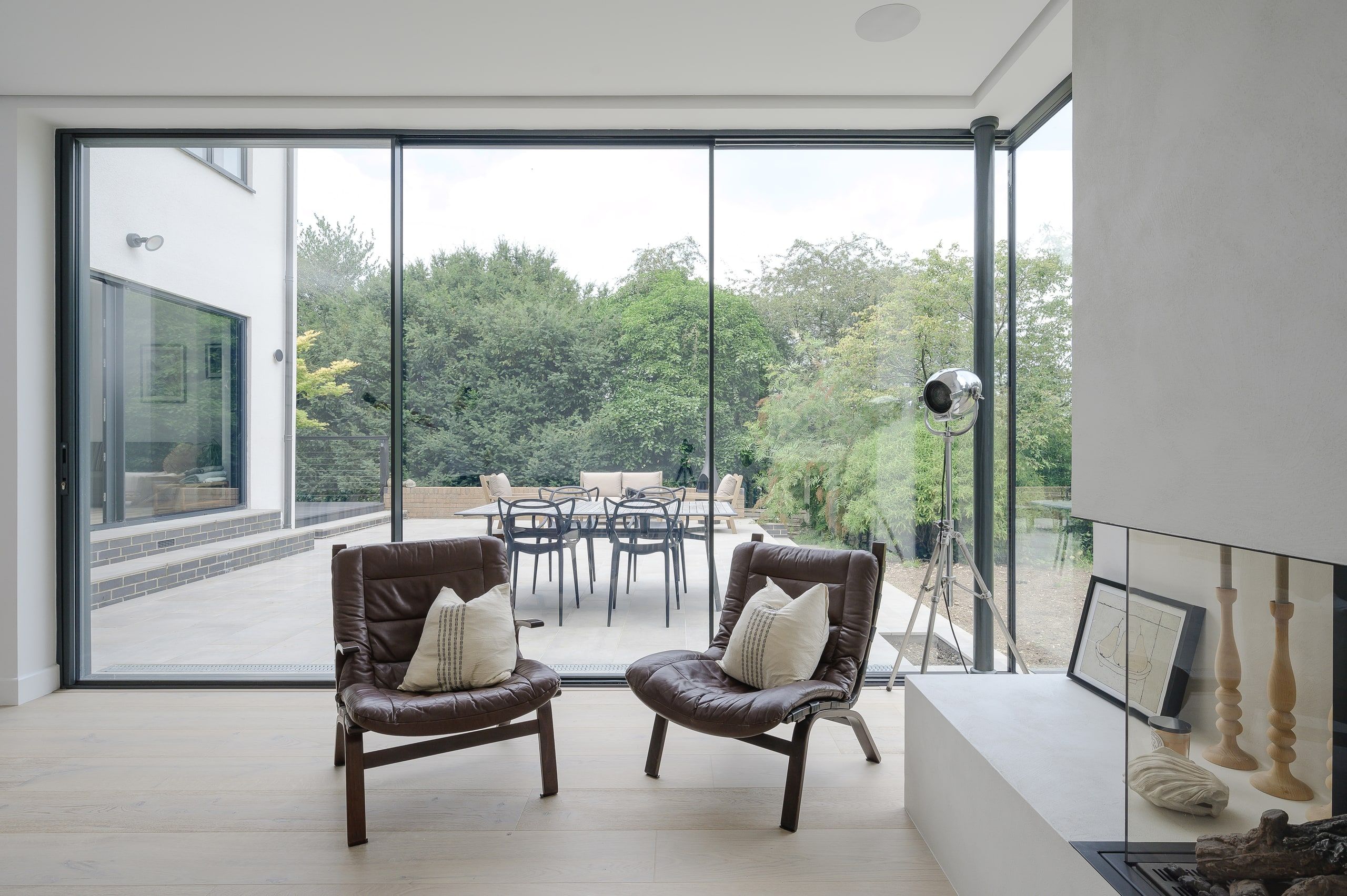 Living room with leather chairs facing full-height sliding doors onto the terrace, 1960s house, Haslemere.