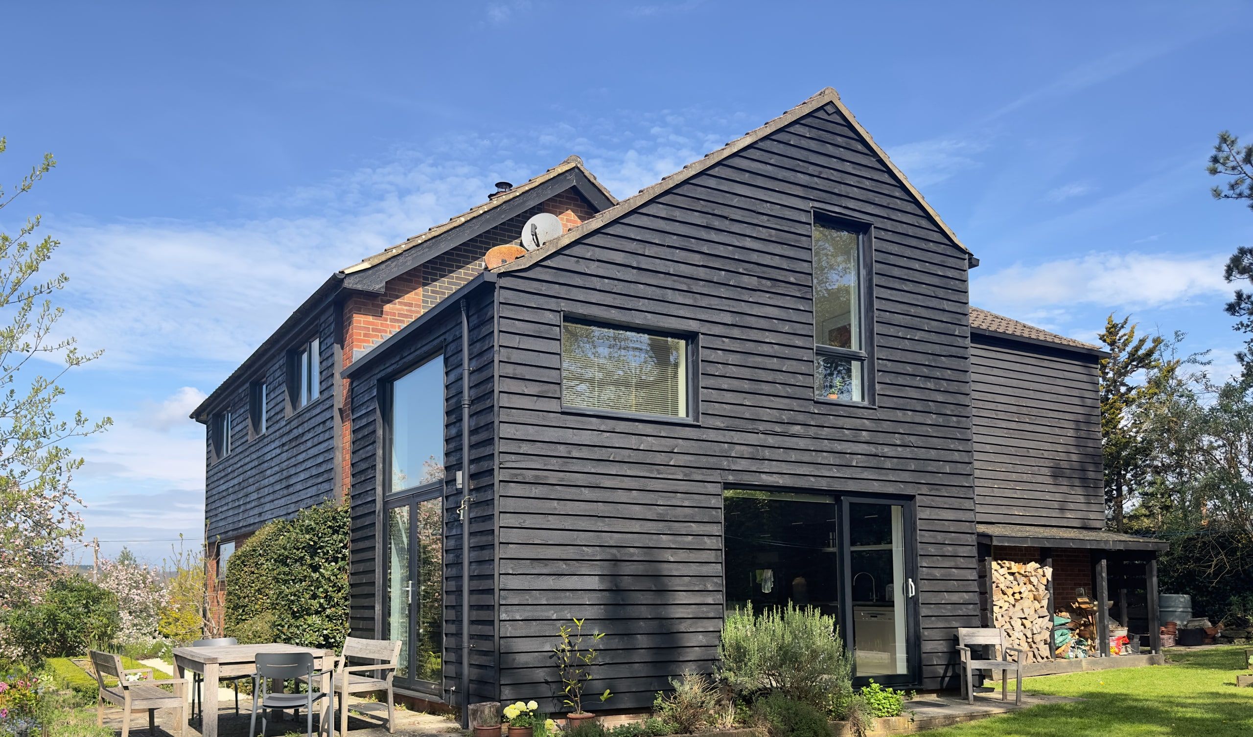 Black timber cladding wrapping the original brick above the garden terrace, 1960s house, Fernhurst.
