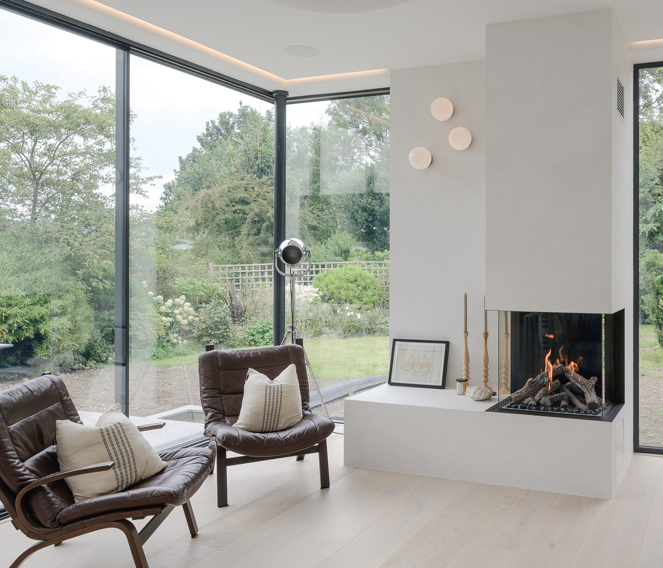 Corner glazing and a white plastered chimney with a lit log fire in the living room, 1960s house, Haslemere.