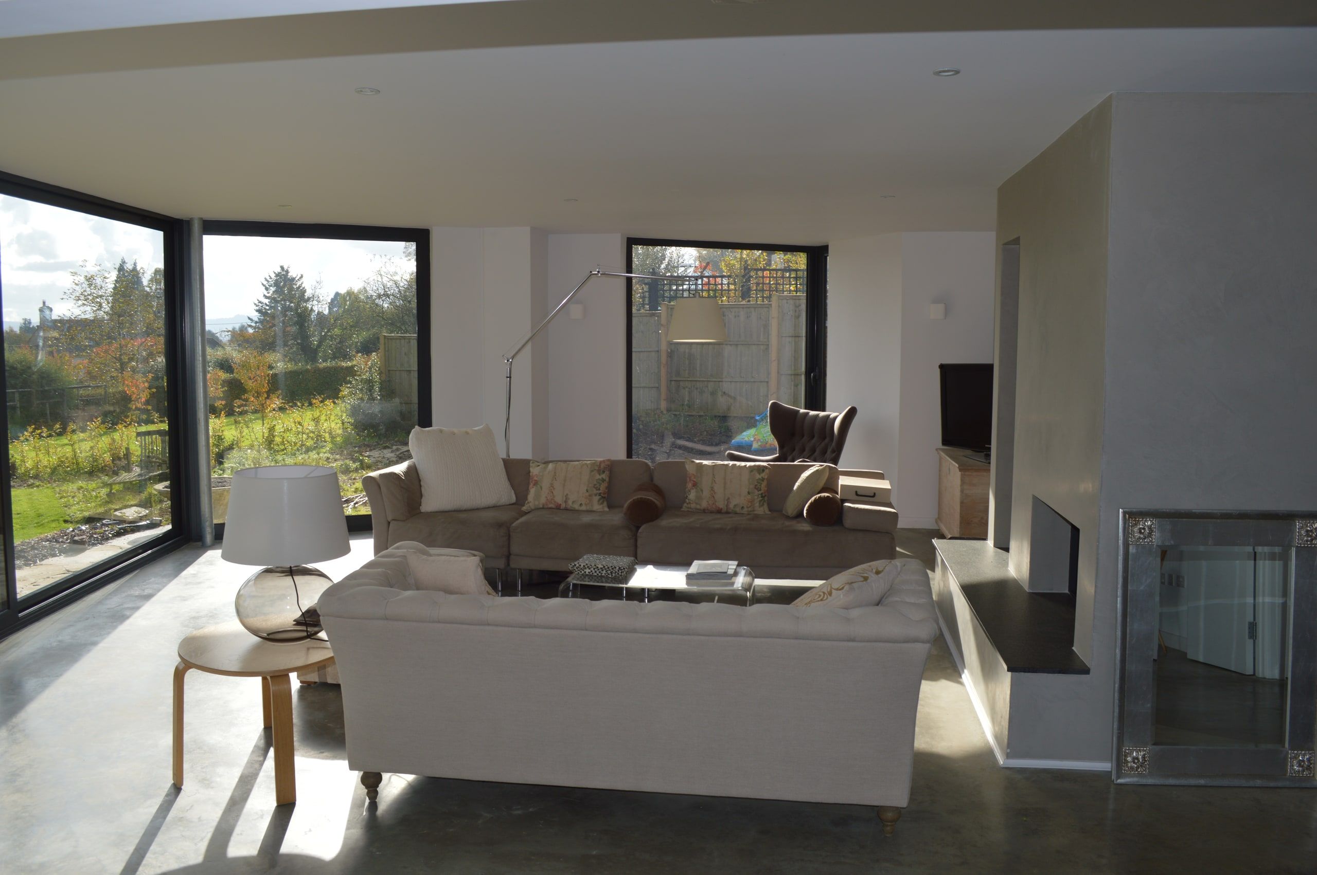 Living room with a double-aspect polished plaster fireplace and garden glazing, 1960s house, Lodsworth.