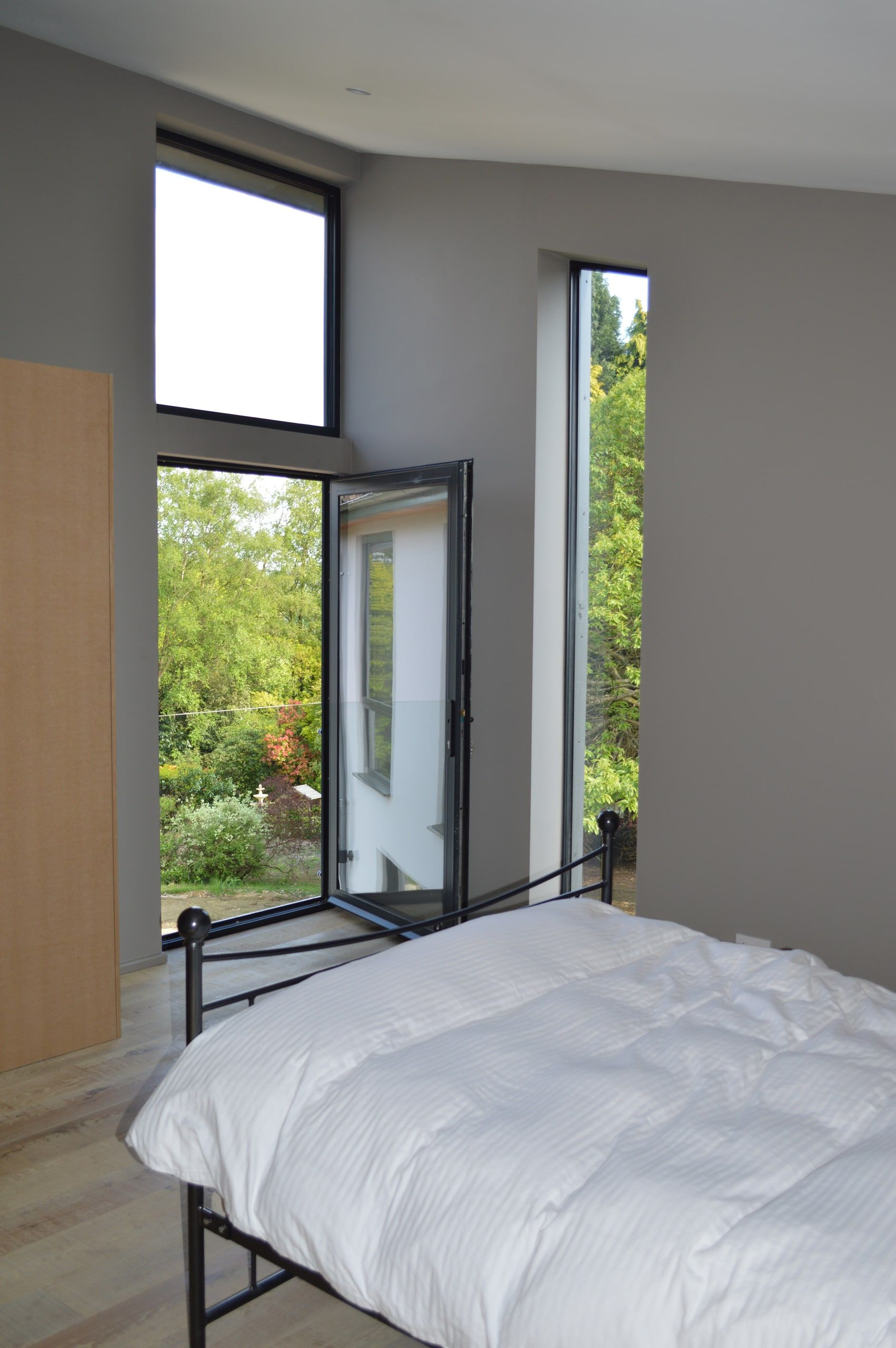 Bedroom with glazed doors and a full-height slot window open to the treetops, 1960s house, Haslemere.