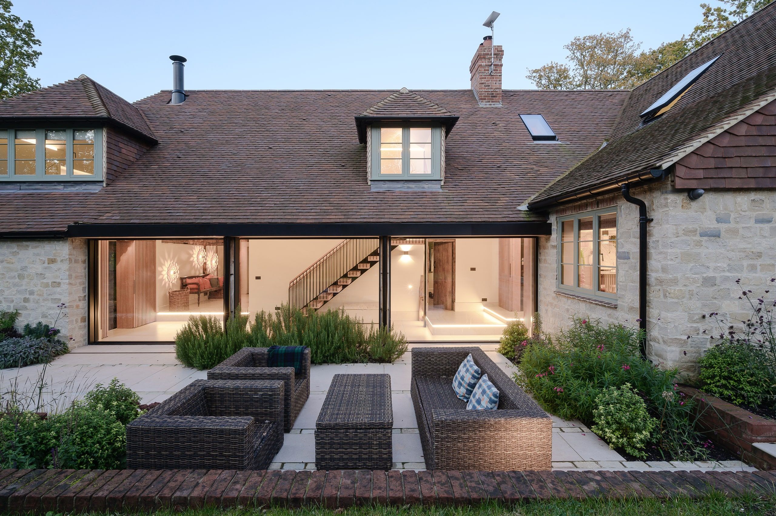 Rear courtyard terrace with rattan seating and sliding glazing into the double-height hall, country house, Lodsworth.
