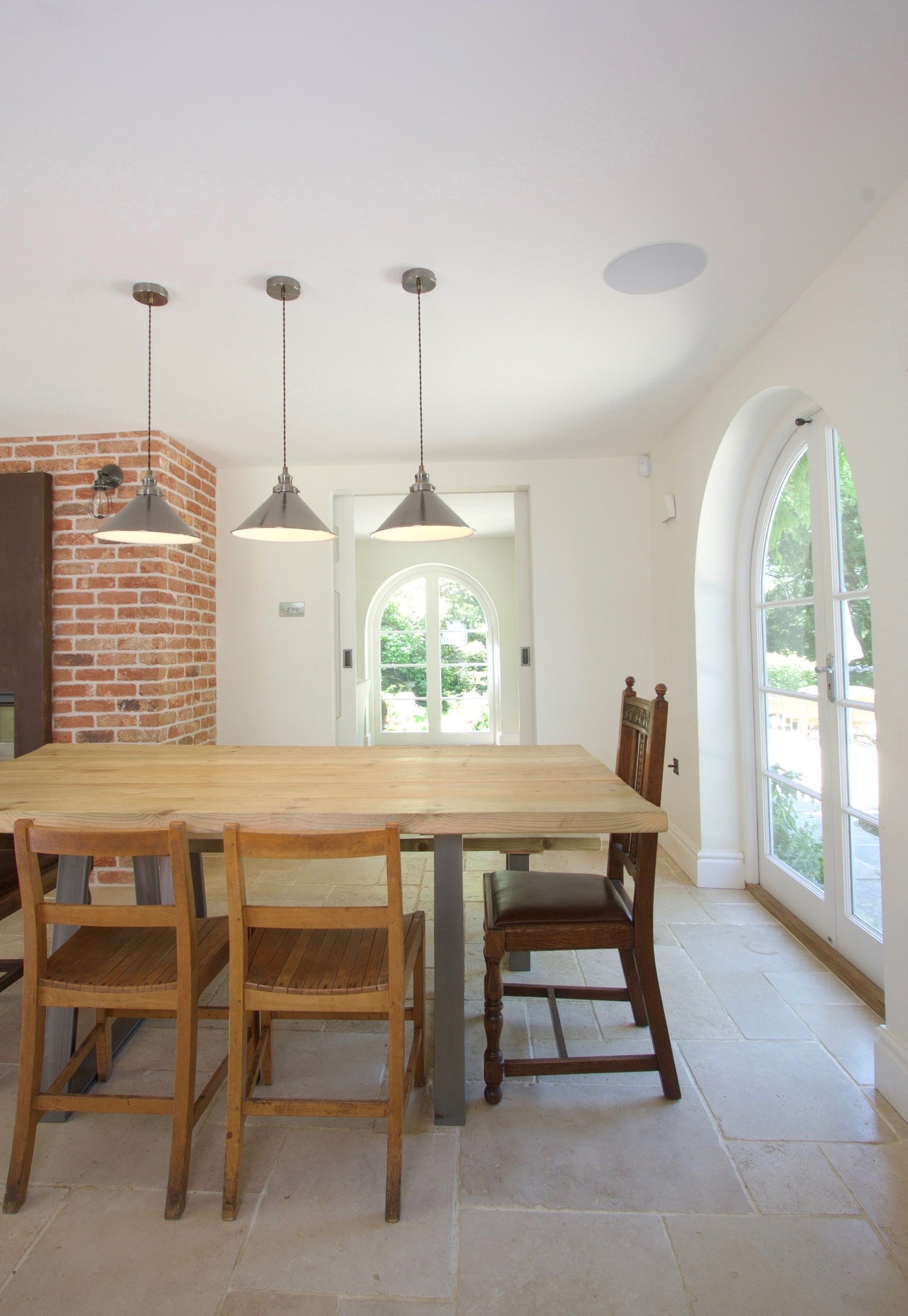 Oak dining table under three pendant lights beside a brick chimney, 1930s country house, Mole Valley.