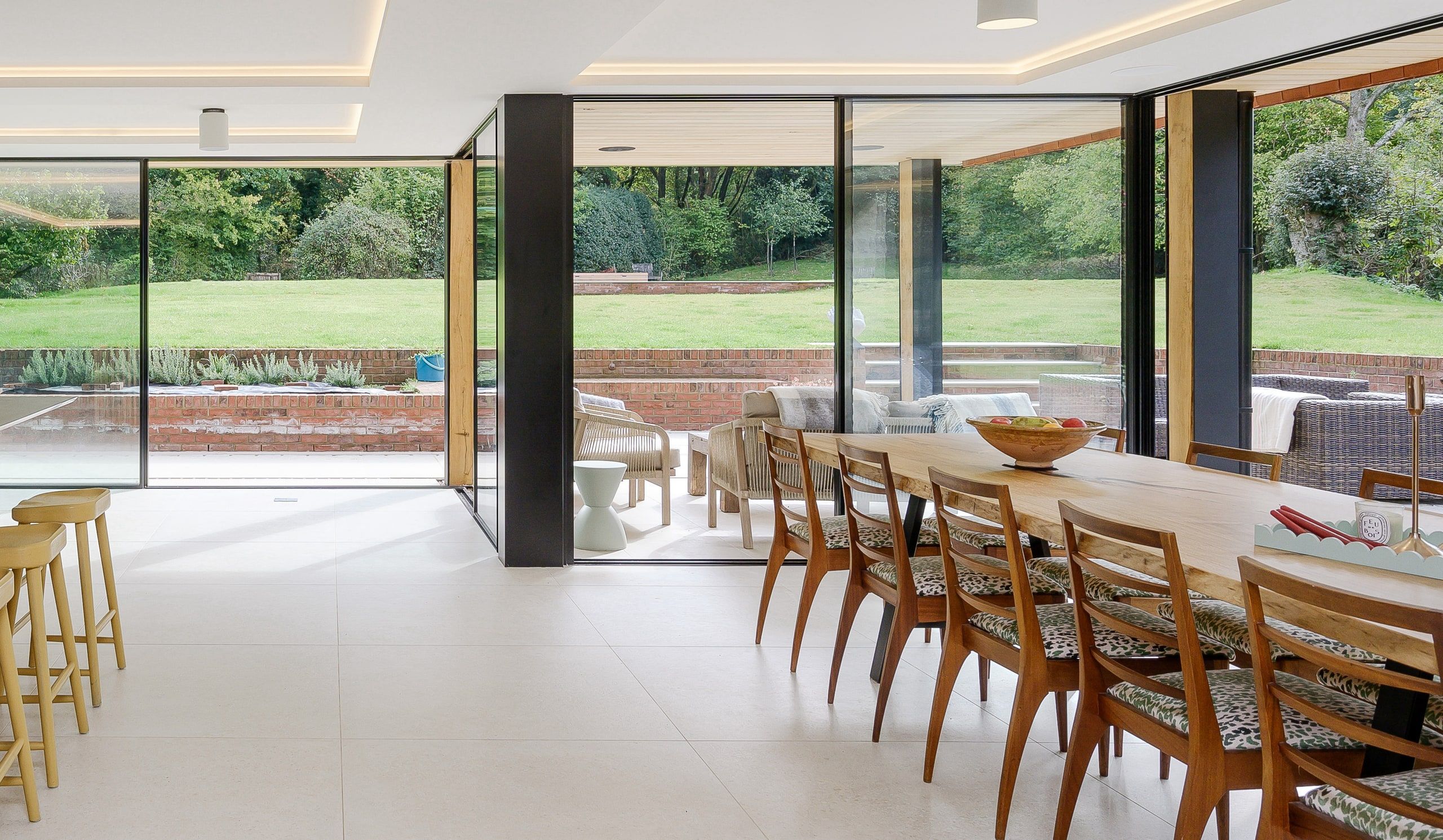 Open-plan dining space with an oak table and full-height corner glazing onto the lawn, country house, Lodsworth.