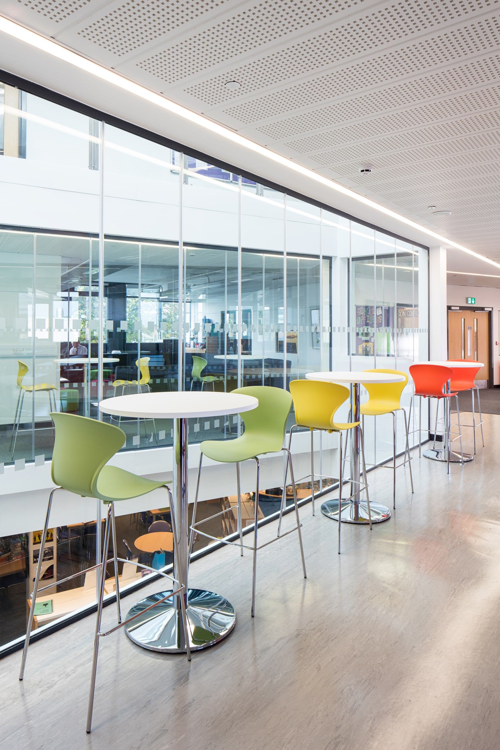 Round white table and bar stools beside the glazed screen of the break-out area, 6th Form Centre, Newbury.