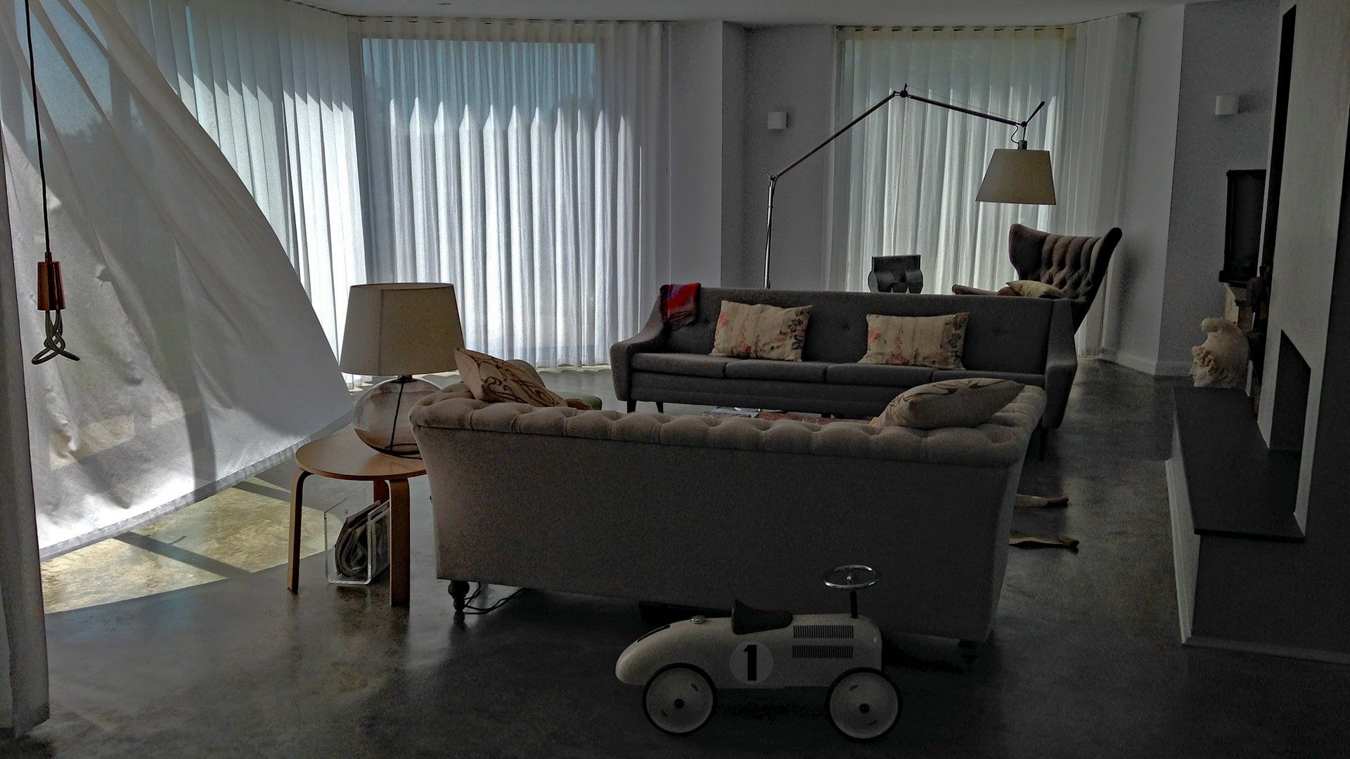 Sofas on the polished concrete floor behind full-height sheer curtains, 1960s house, Lodsworth.