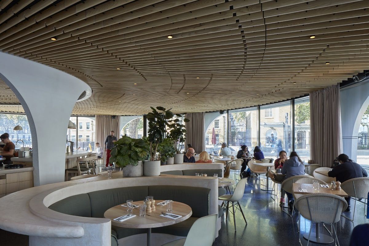 Curved banquette and tables beneath the ribbed timber ceiling, restaurant pavilion, Duke of York Square, London.