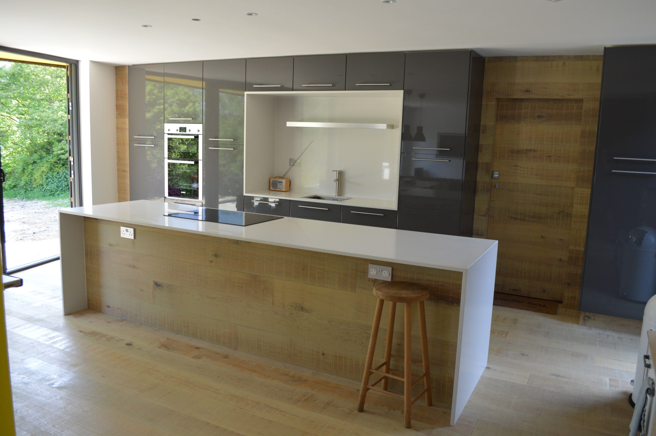 Oak-fronted island and grey gloss units, with doors folded open to the garden, 1960s house, Haslemere.