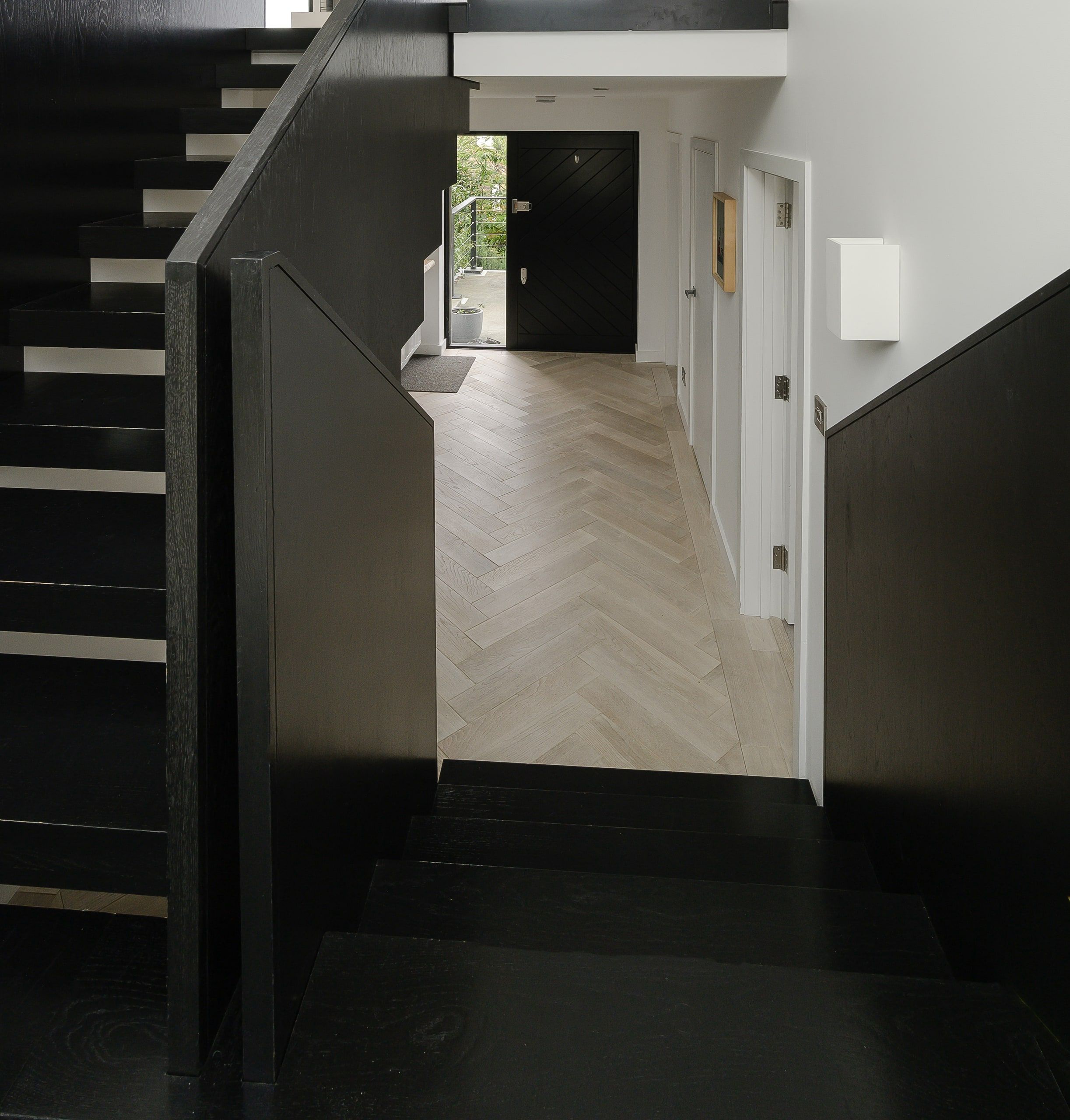 Black timber stair and balustrade framing the hall and the new front door, upside down house, Haslemere.
