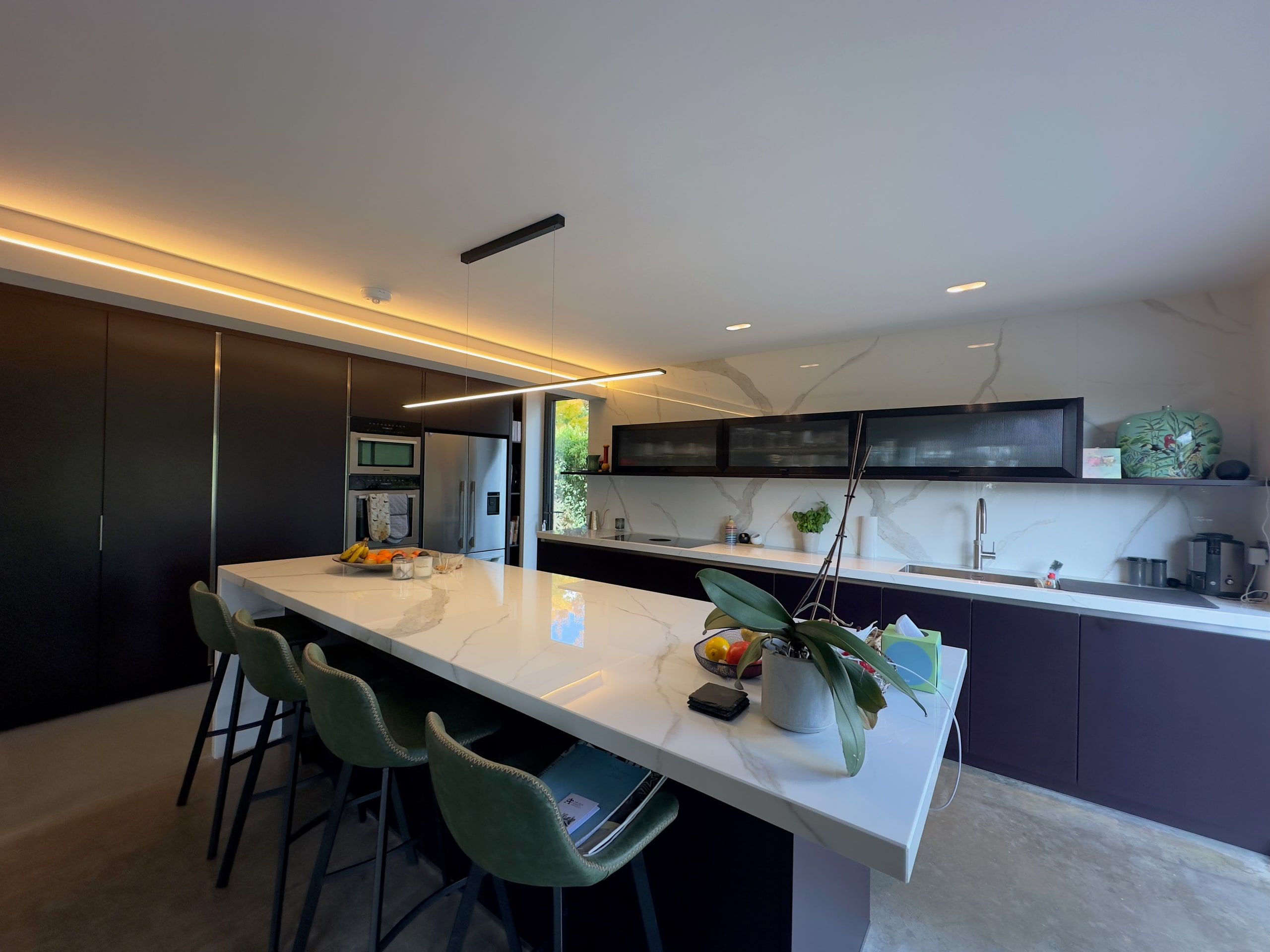 Kitchen island and breakfast bar stools beside dark full-height units, 1960s house, Lodsworth.