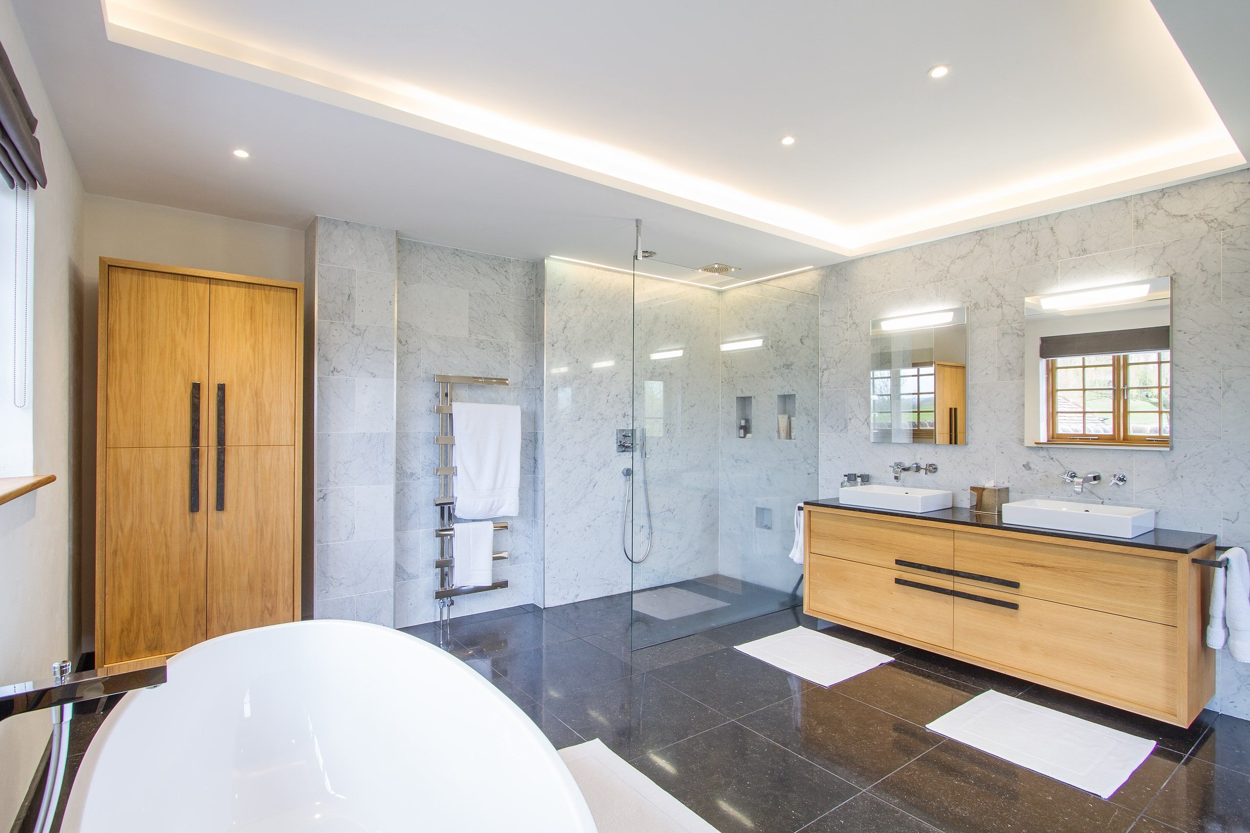 Master bathroom with a walk-in shower, twin oak vanity and dark stone floor, listed country house, Chiddingfold.