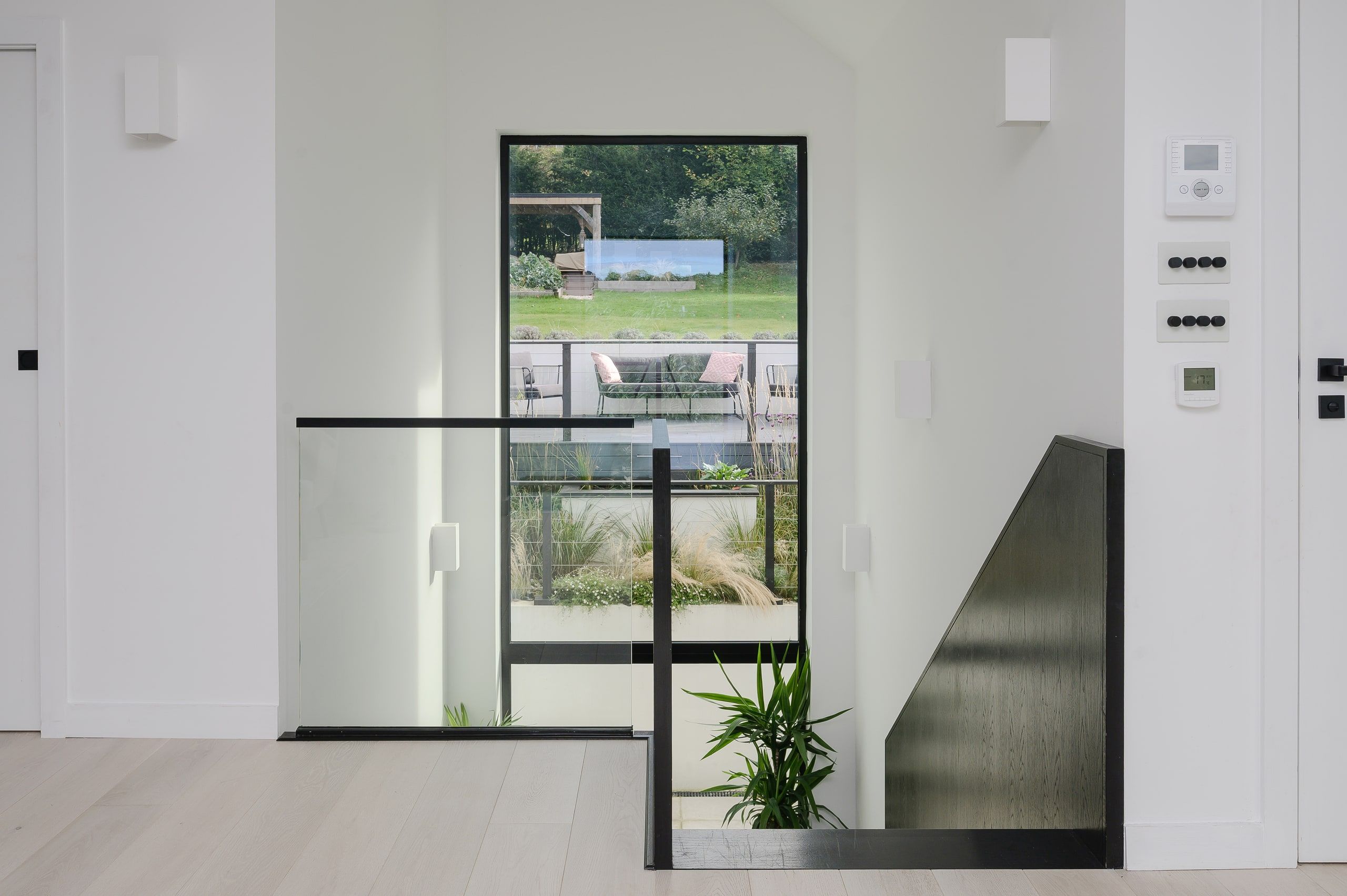 First-floor landing with a glass balustrade and a tall window onto the terrace, upside down house, Haslemere.