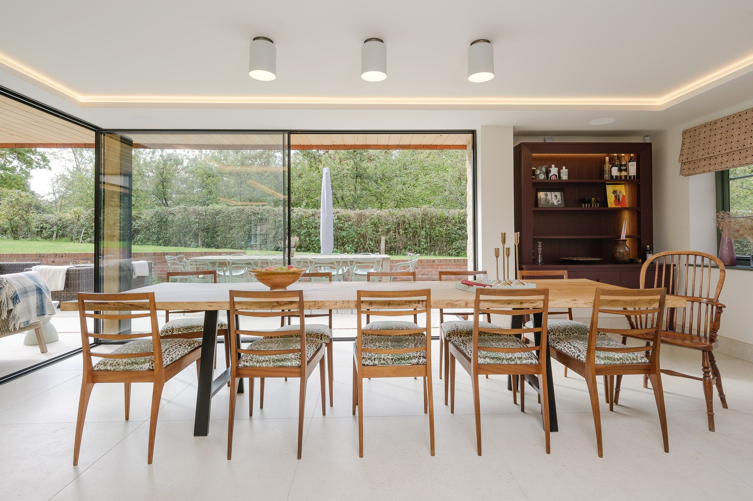 Long dining room under a cove-lit ceiling with garden glazing along one side, country house, Lodsworth.