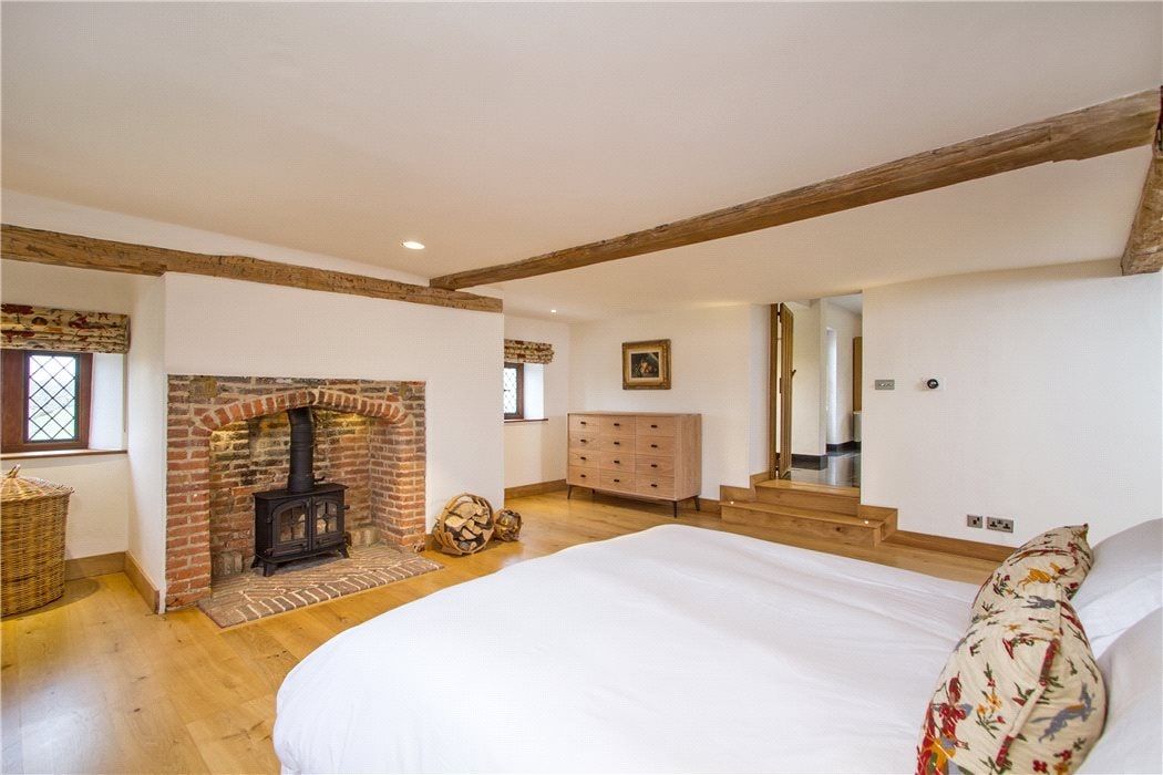 Bedroom with a brick fireplace and wood-burning stove on a wide oak floor, listed country house, Chiddingfold.