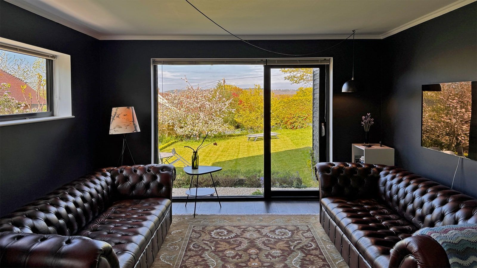 Leather chesterfields facing the garden in the dark-painted snug, 1960s house, Fernhurst.