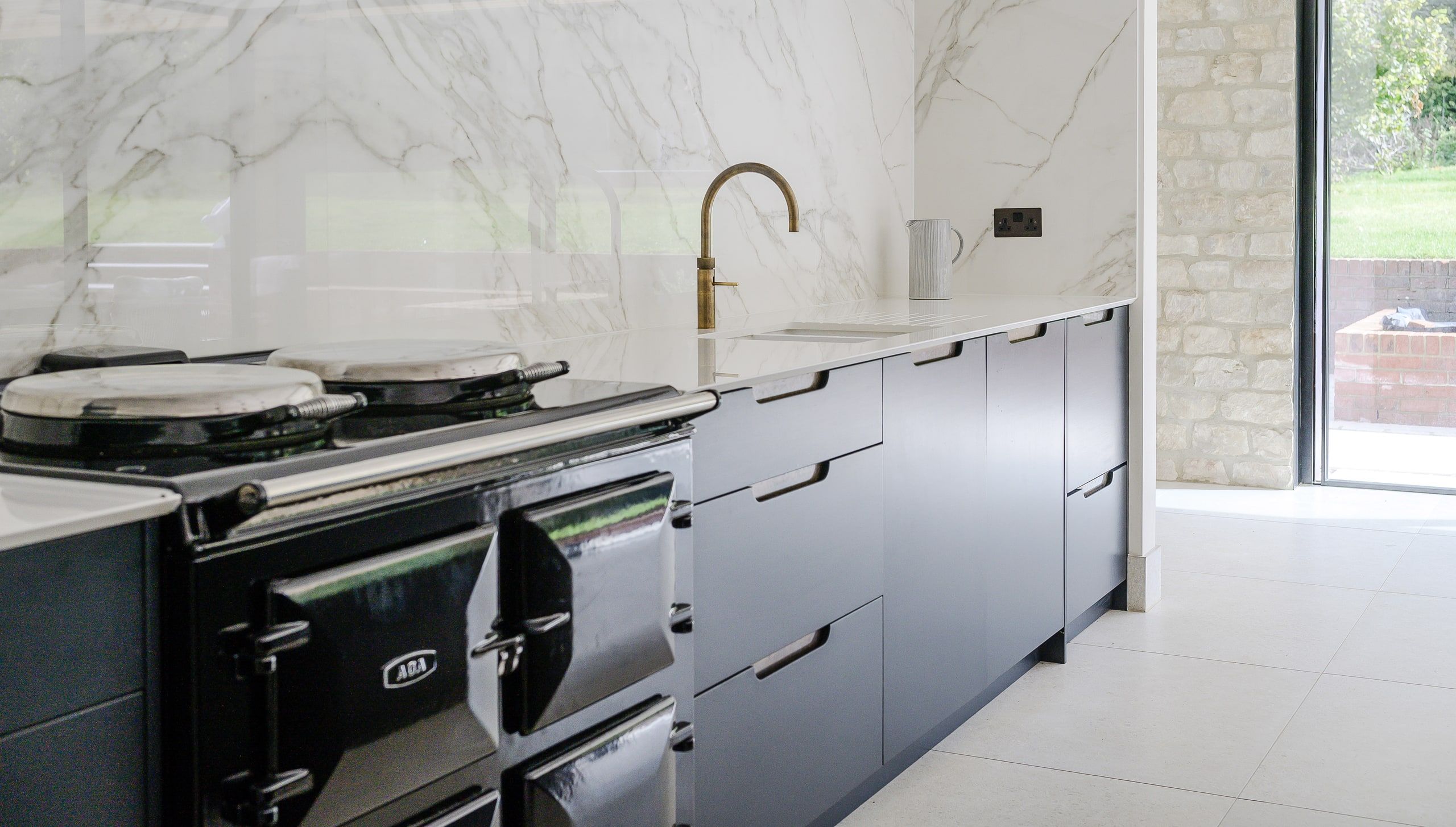 Cast-iron range cooker and brass tap against a veined marble splashback, country house, Lodsworth.