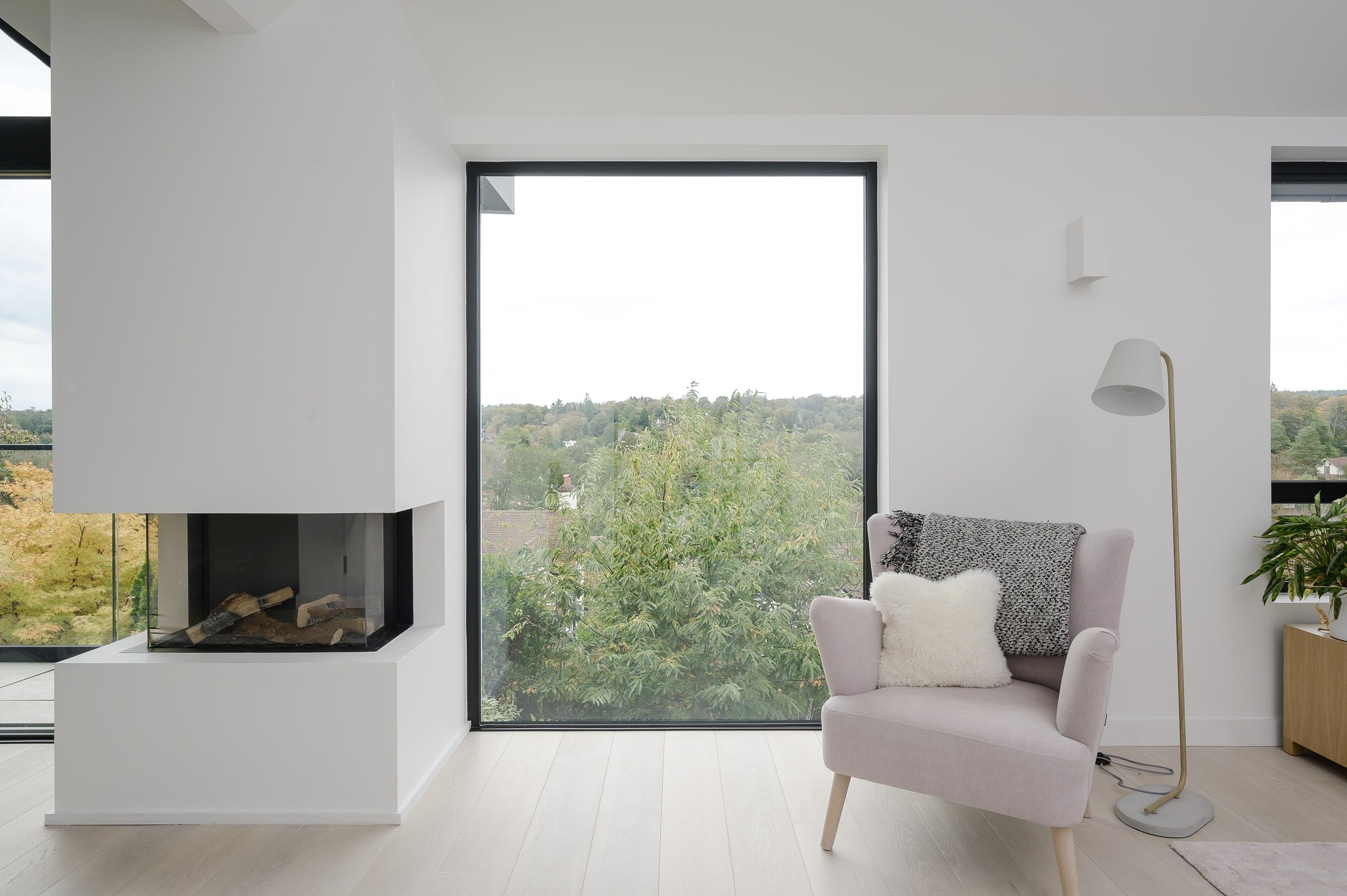Living room with a corner log fire and a tall window over the treetops, upside down house, Haslemere.