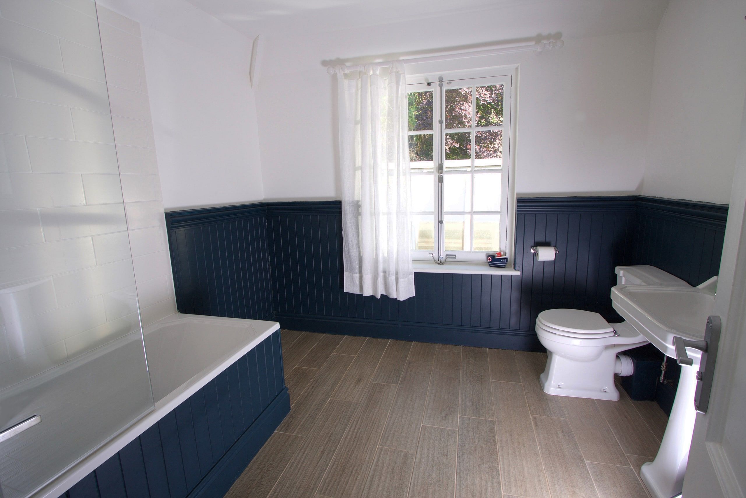 Family bathroom with a panelled bath and navy tongue-and-groove dado, 1930s country house, Mole Valley.