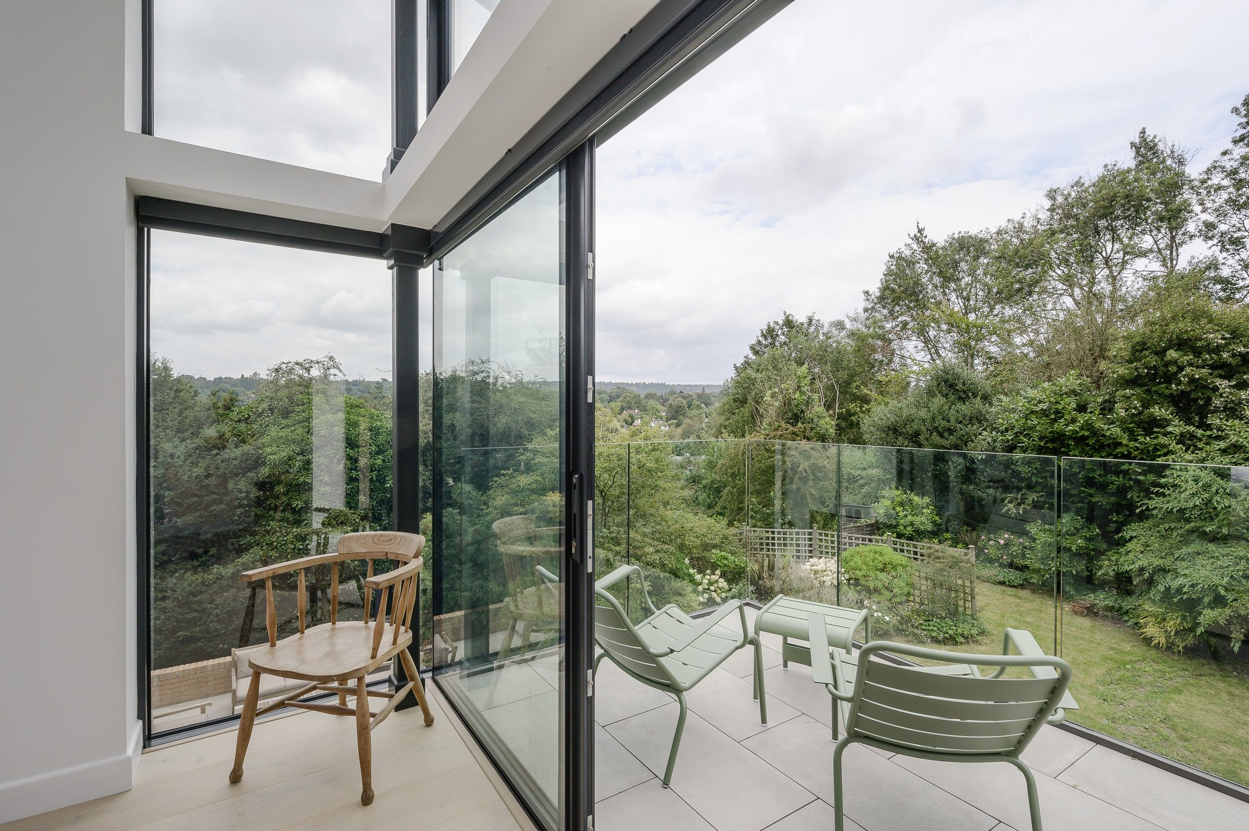 Roof terrace seen from inside, with a glass balustrade and long views over the trees, 1960s house, Haslemere.