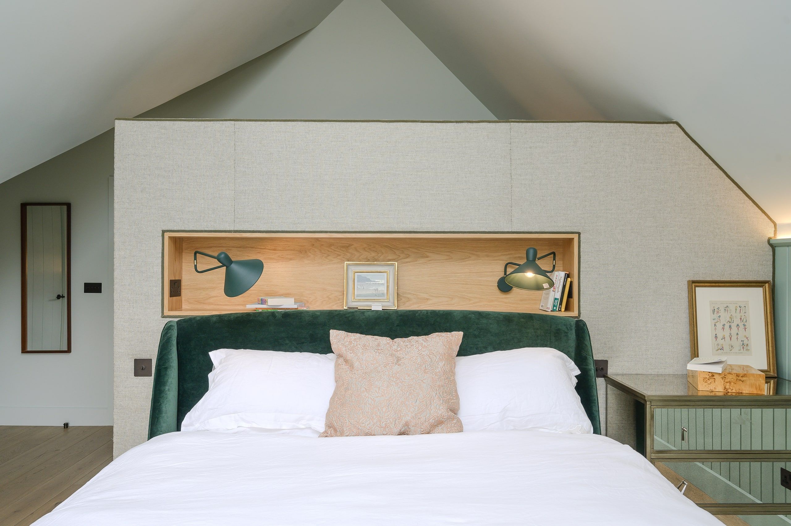 Bedroom under a vaulted ceiling with a green velvet bed and oak-lined headboard recess, country house, Lodsworth.