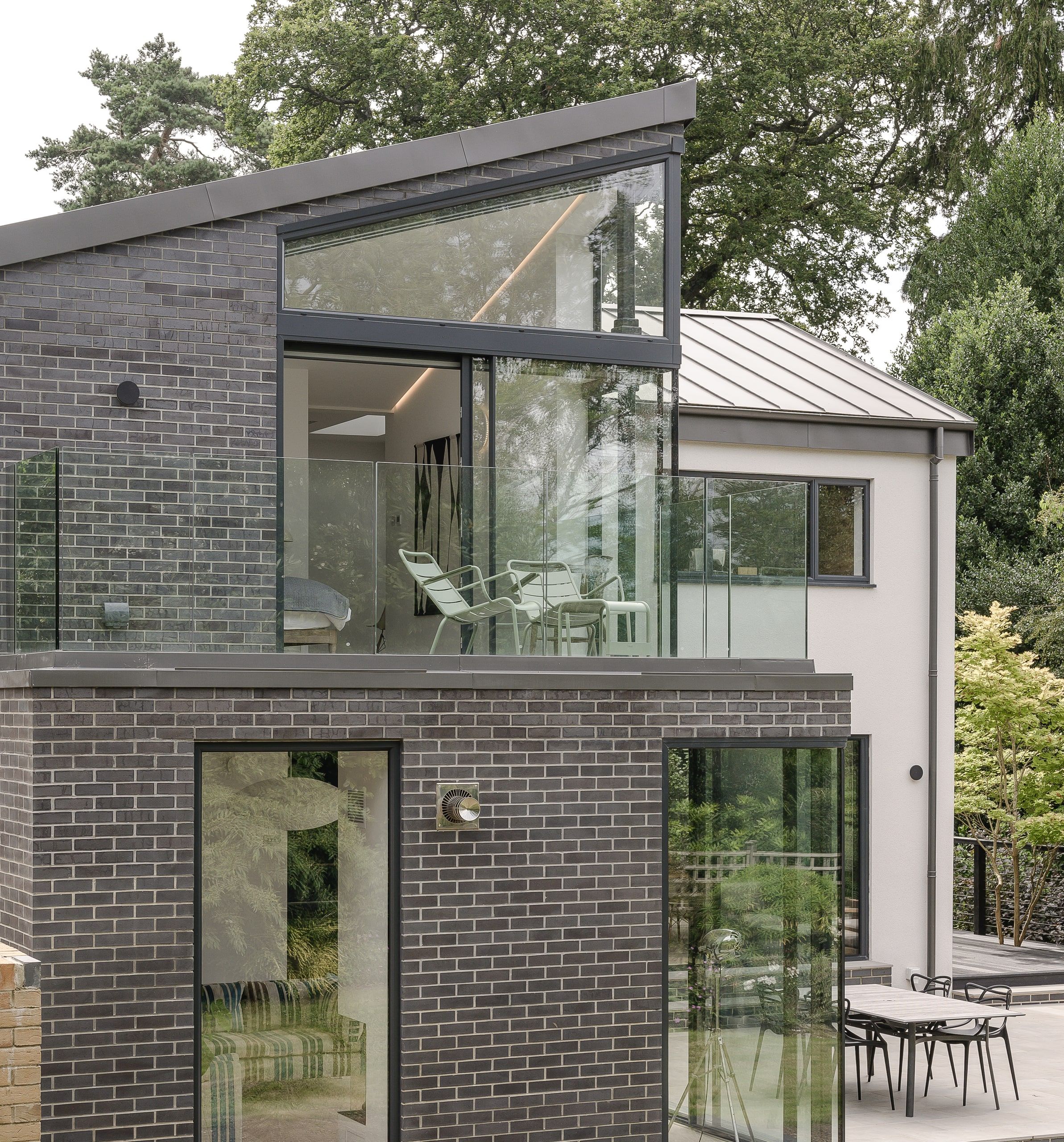 Two-storey brick and rendered rear elevation with a zinc roof and glass balcony, 1960s house, Haslemere.