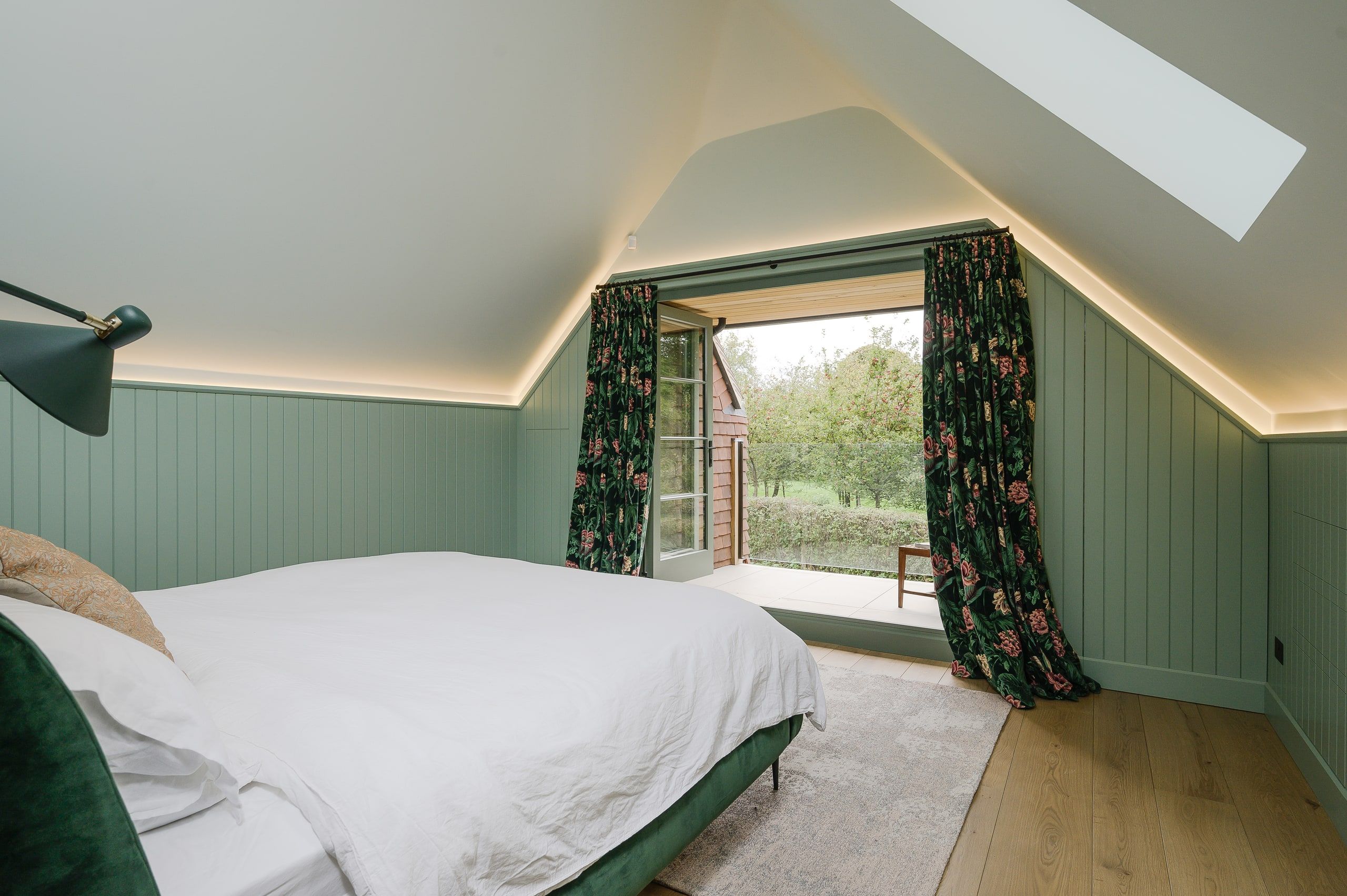 Attic guest bedroom with sage panelling, a rooflight and doors onto a small balcony, country house, Lodsworth.