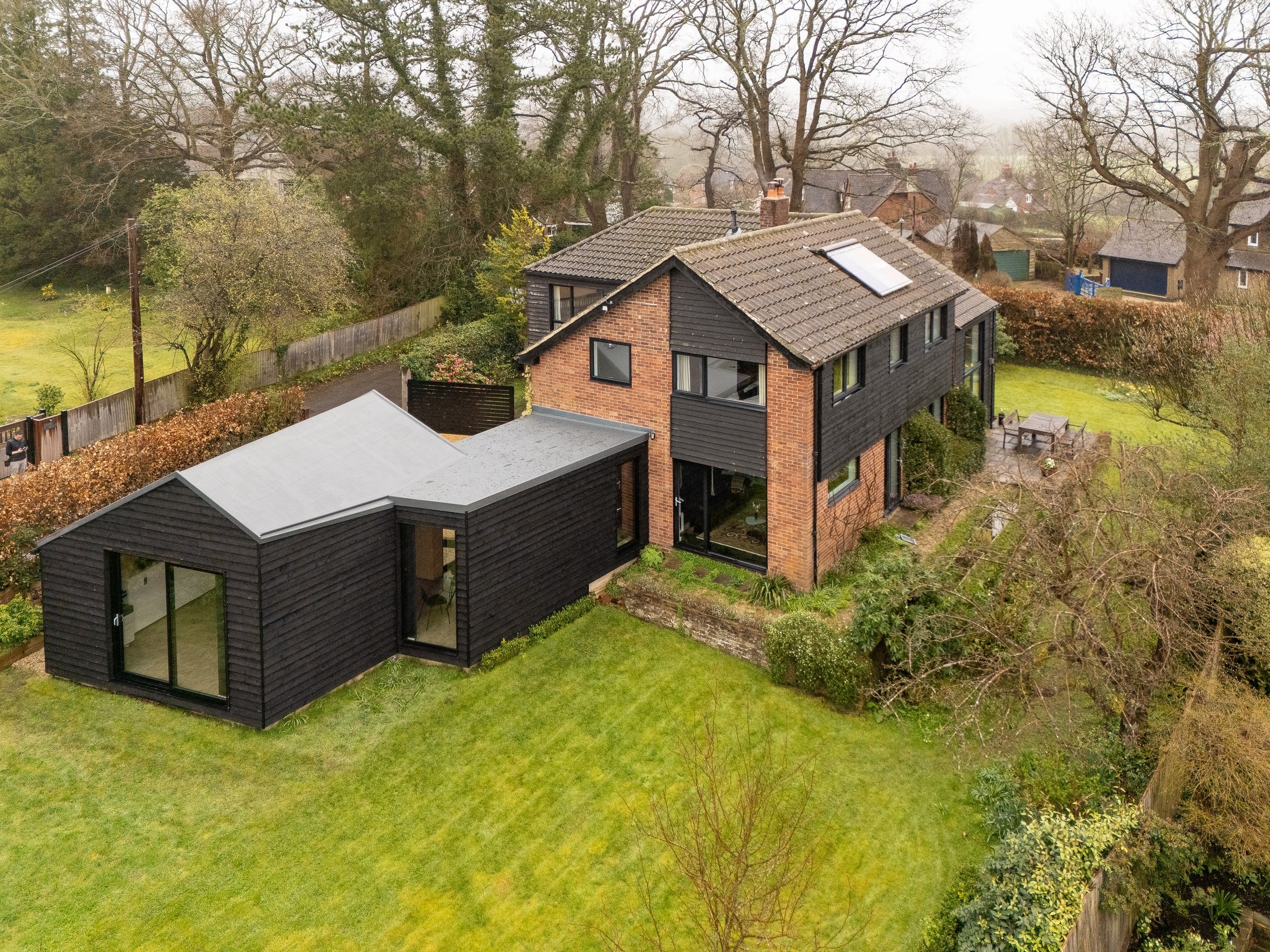 Aerial view of the flat-roofed black timber extension against the brick house, 1960s house, Fernhurst.